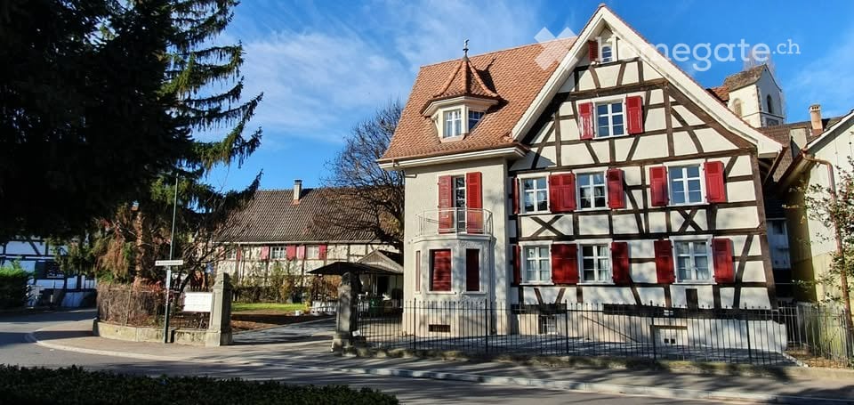 Two story house, red roof, red shutters, front gate, red shutters, surrounded by trees
