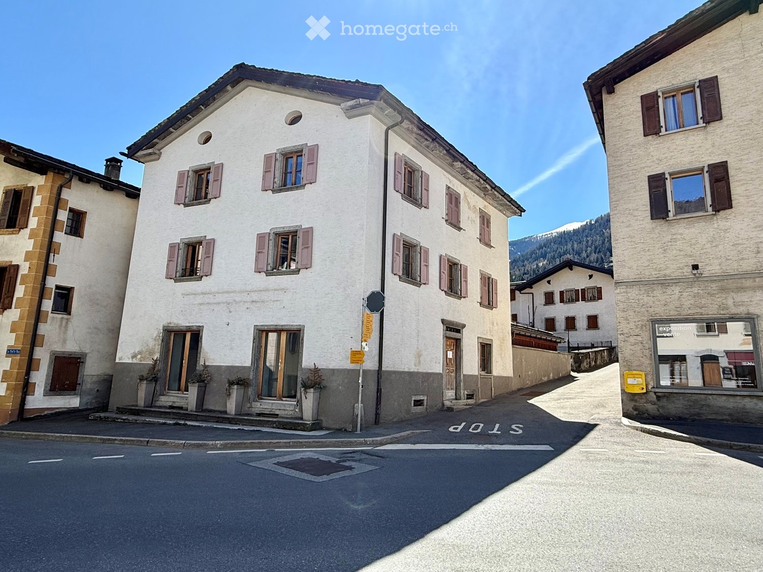 3 story building, white exterior, multiple windows, street sign, potted plants, mountains in the background