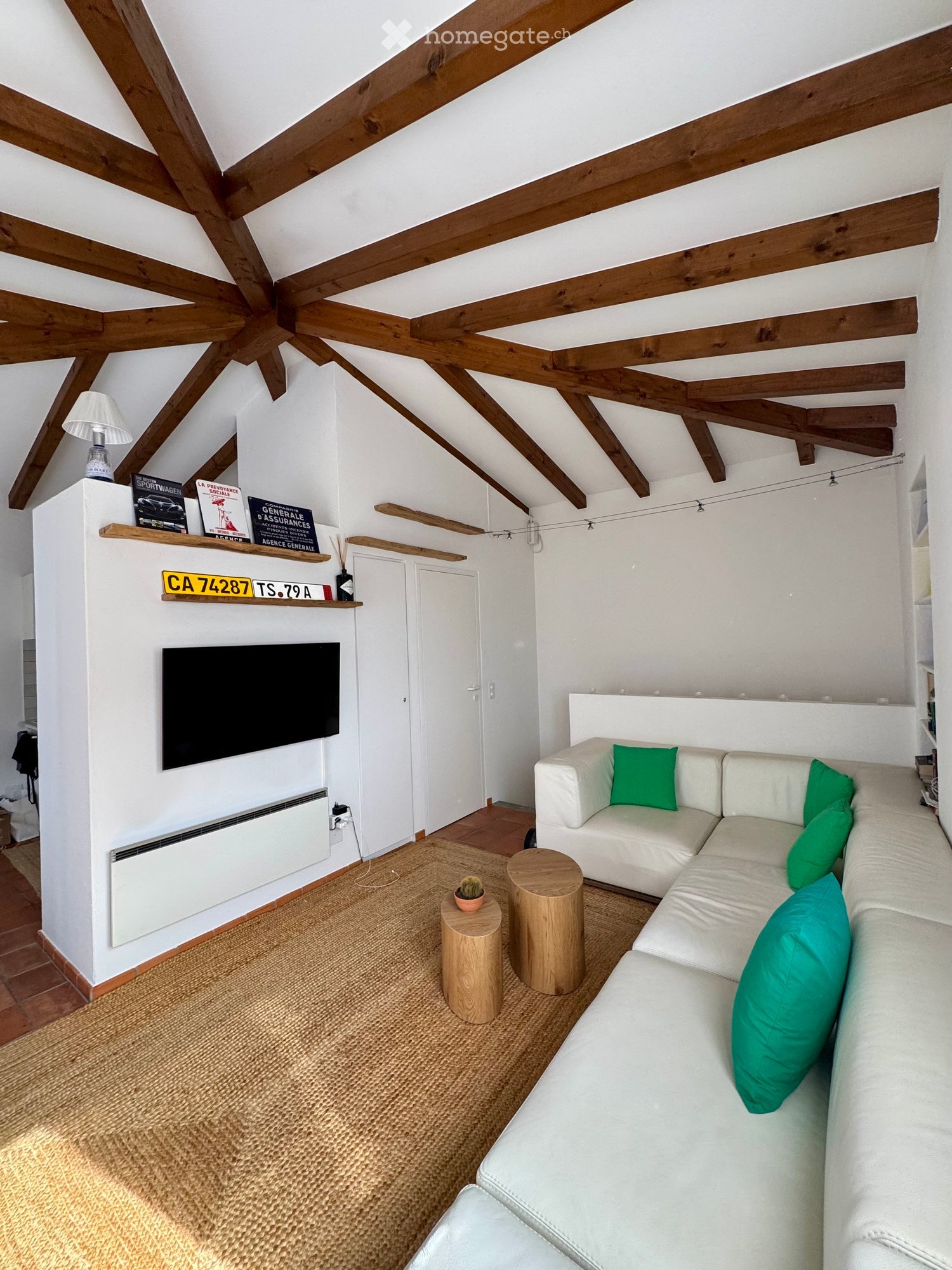 living room with wooden beams, white walls, beige carpet, white sofa, green pillows, wooden coffee tables, flat screen TV, radiator