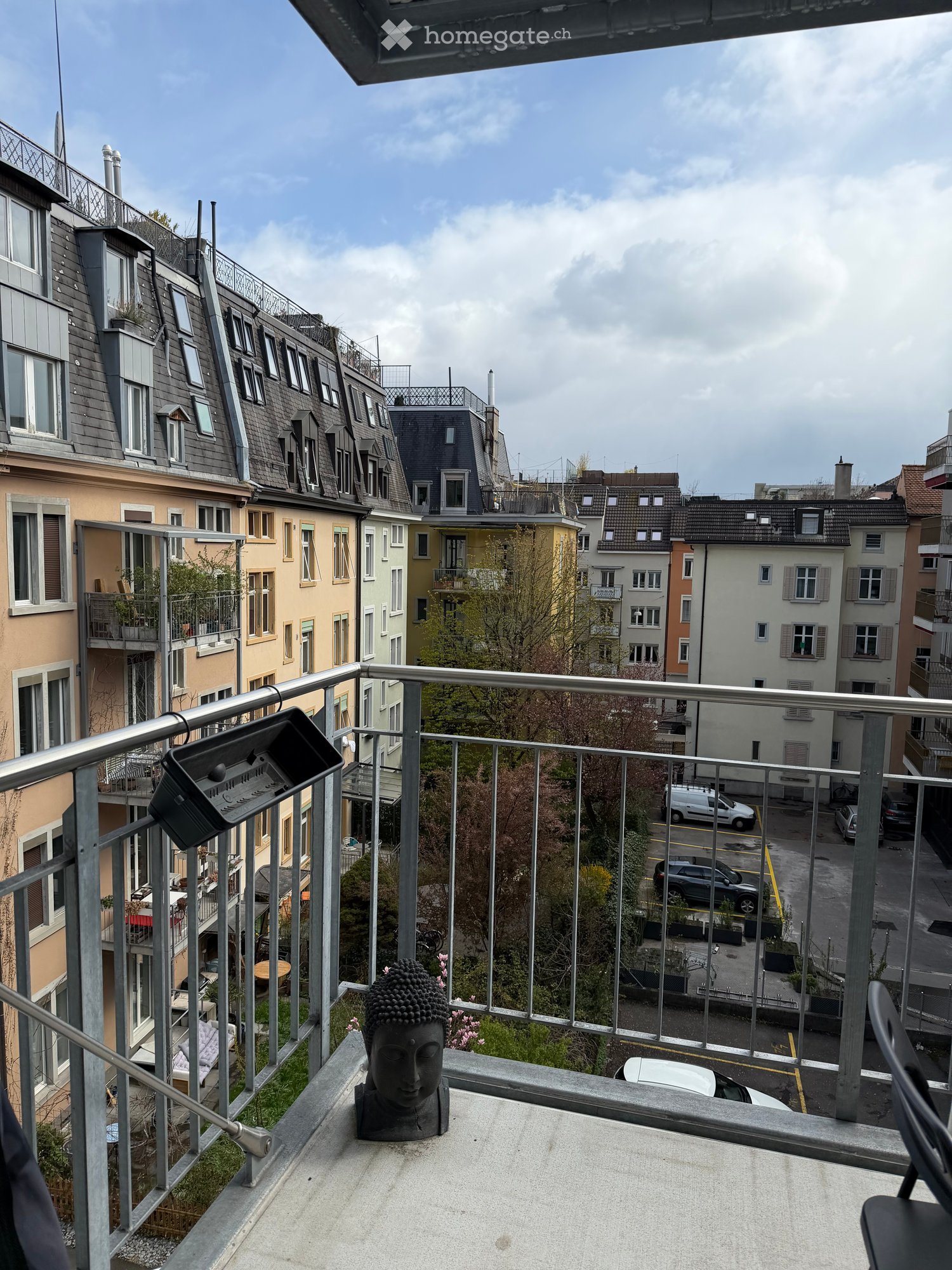 Balcony with metal railings, Buddha statue, plants, and a view of the street and buildings
