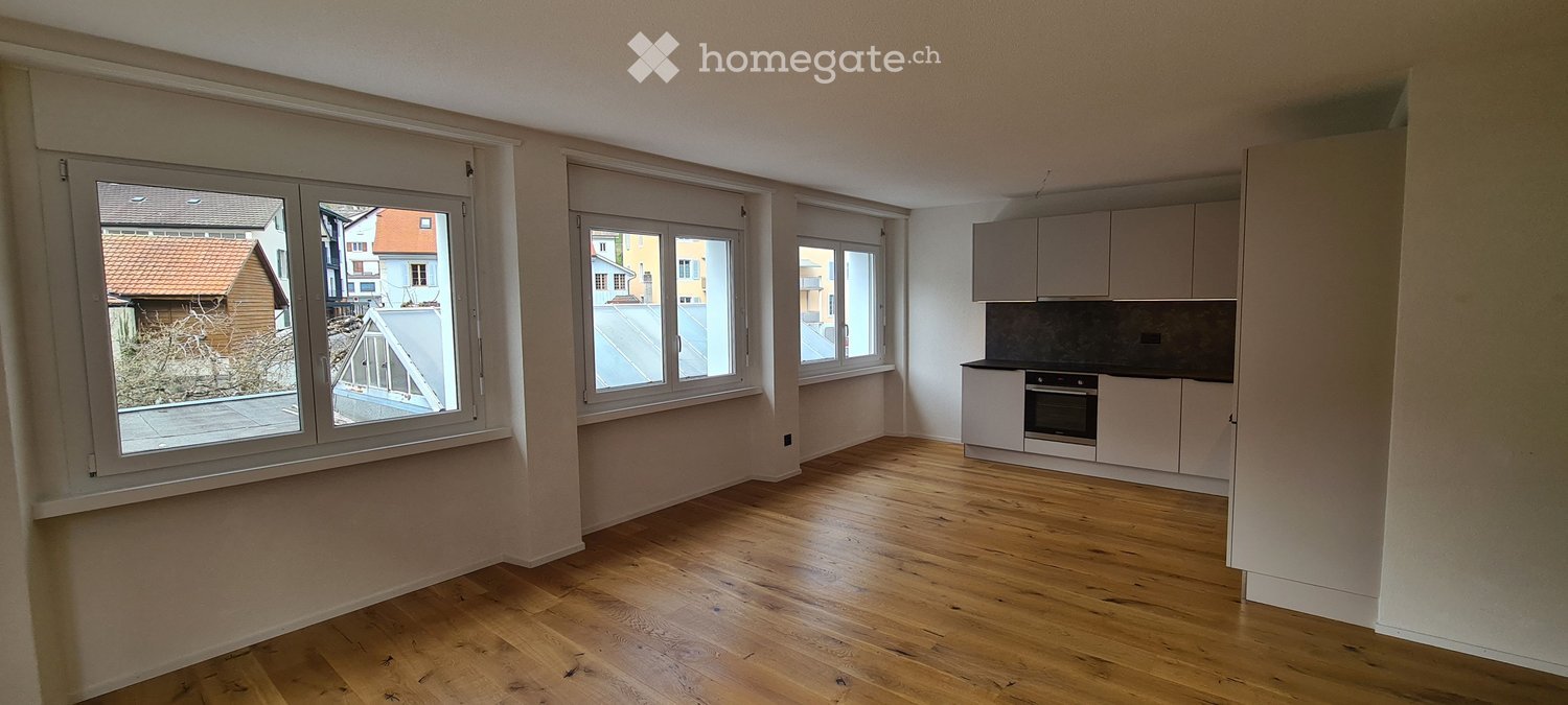 empty room, wooden floor, white walls, three windows, kitchen with oven and cabinets