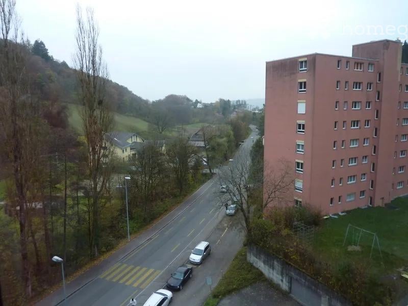 Aerial view of a building with multiple windows, cars parked on the side of the road, and a grassy area with a swing set.