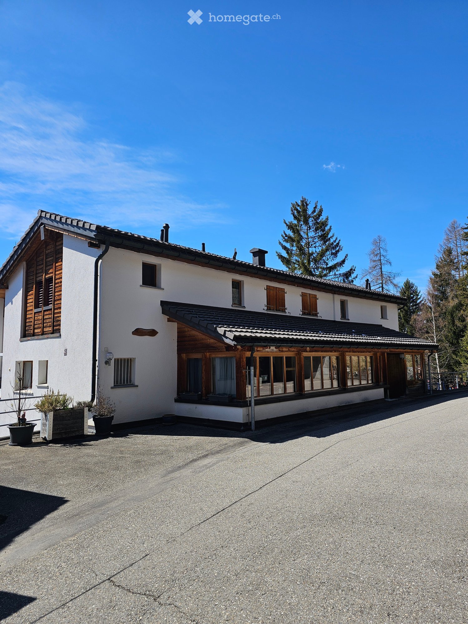 2 story house, white walls, brown wooden trim, large windows, black roof, large driveway, 3 potted plants