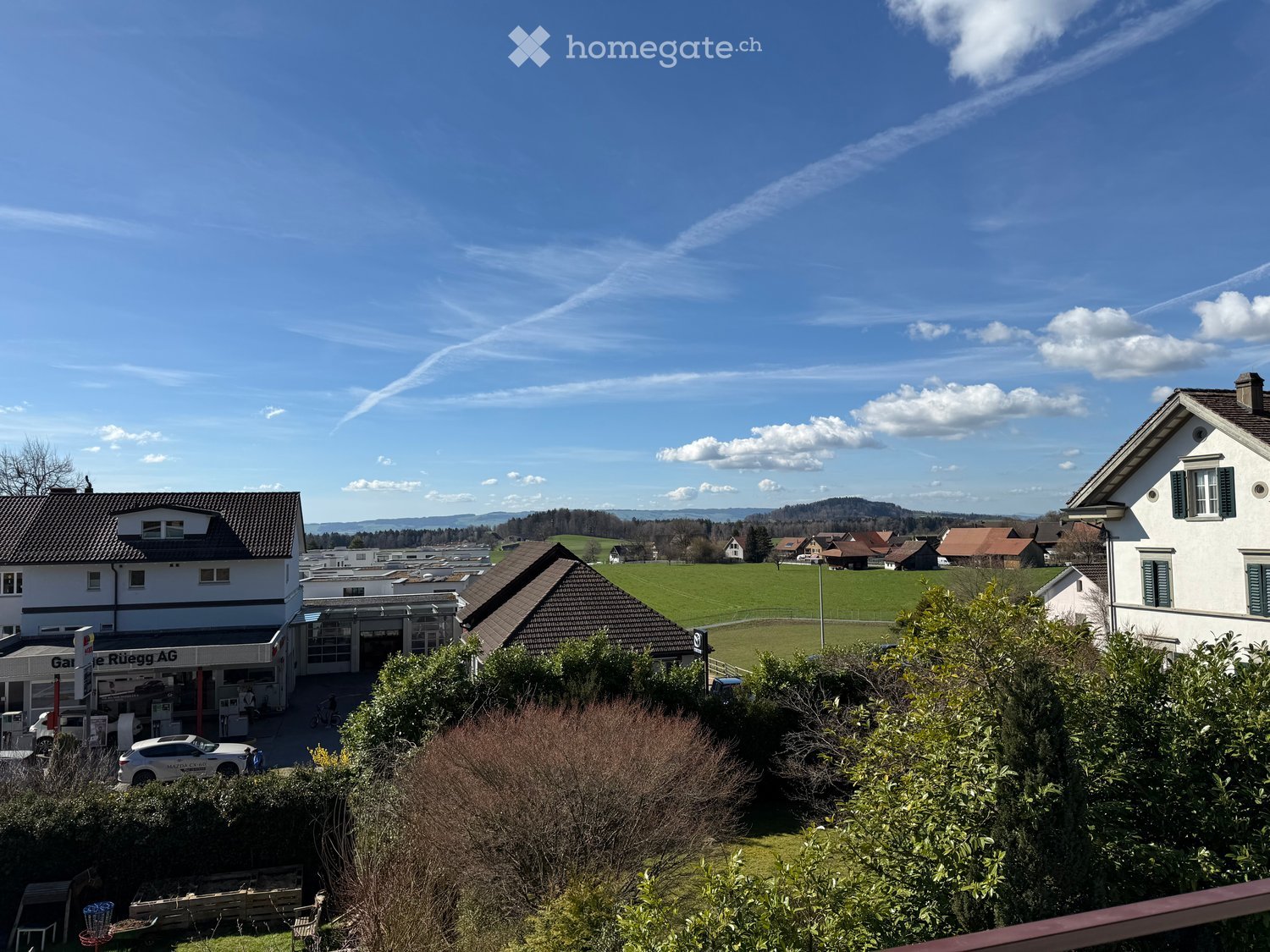Aerial view of a neighborhood with houses, a field, and a clear blue sky with clouds