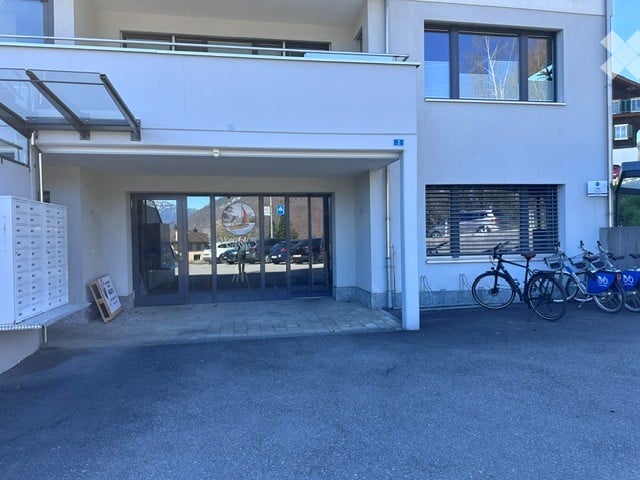 white building, glass entrance, bicycles parked, parking lot