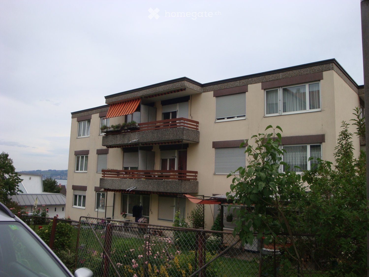 3-story building, beige walls, balconies on multiple levels, awnings