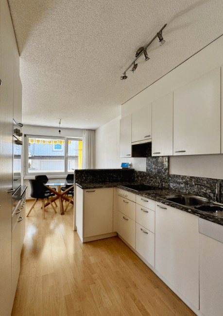 modern kitchen with white cabinets, wooden floor, granite countertops, stainless steel sink, dining table, window with curtains