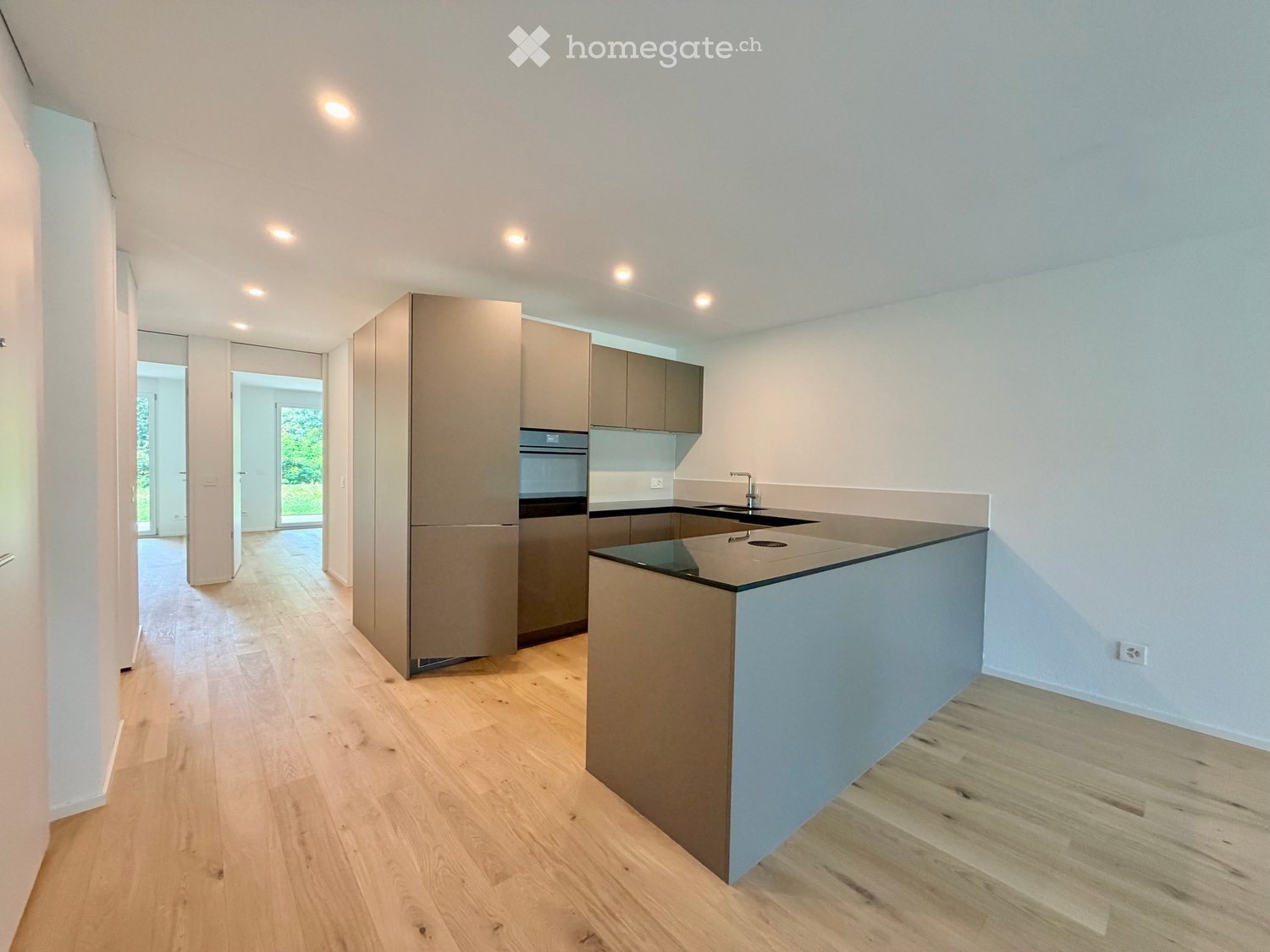 Modern kitchen with light wood flooring, grey cabinets, a central island, and built-in appliances.