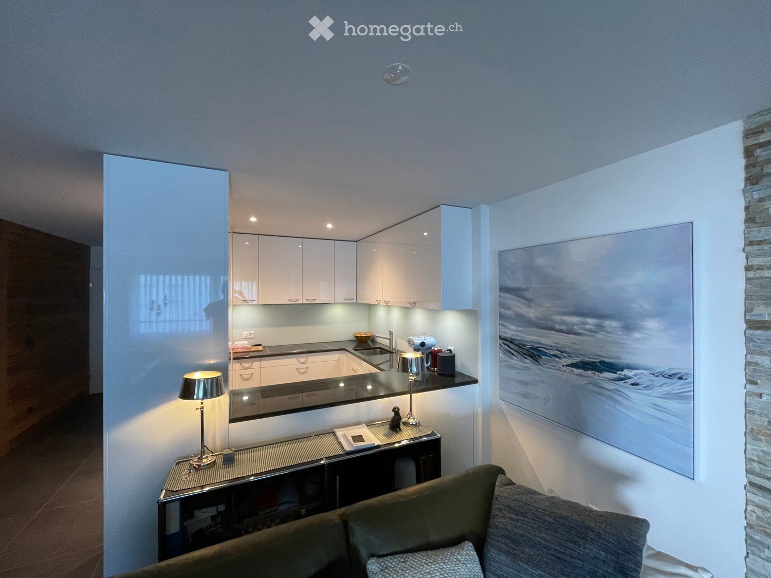 modern kitchen with white cabinets, black countertops, a sink, a lamp, a couch, and a large painting