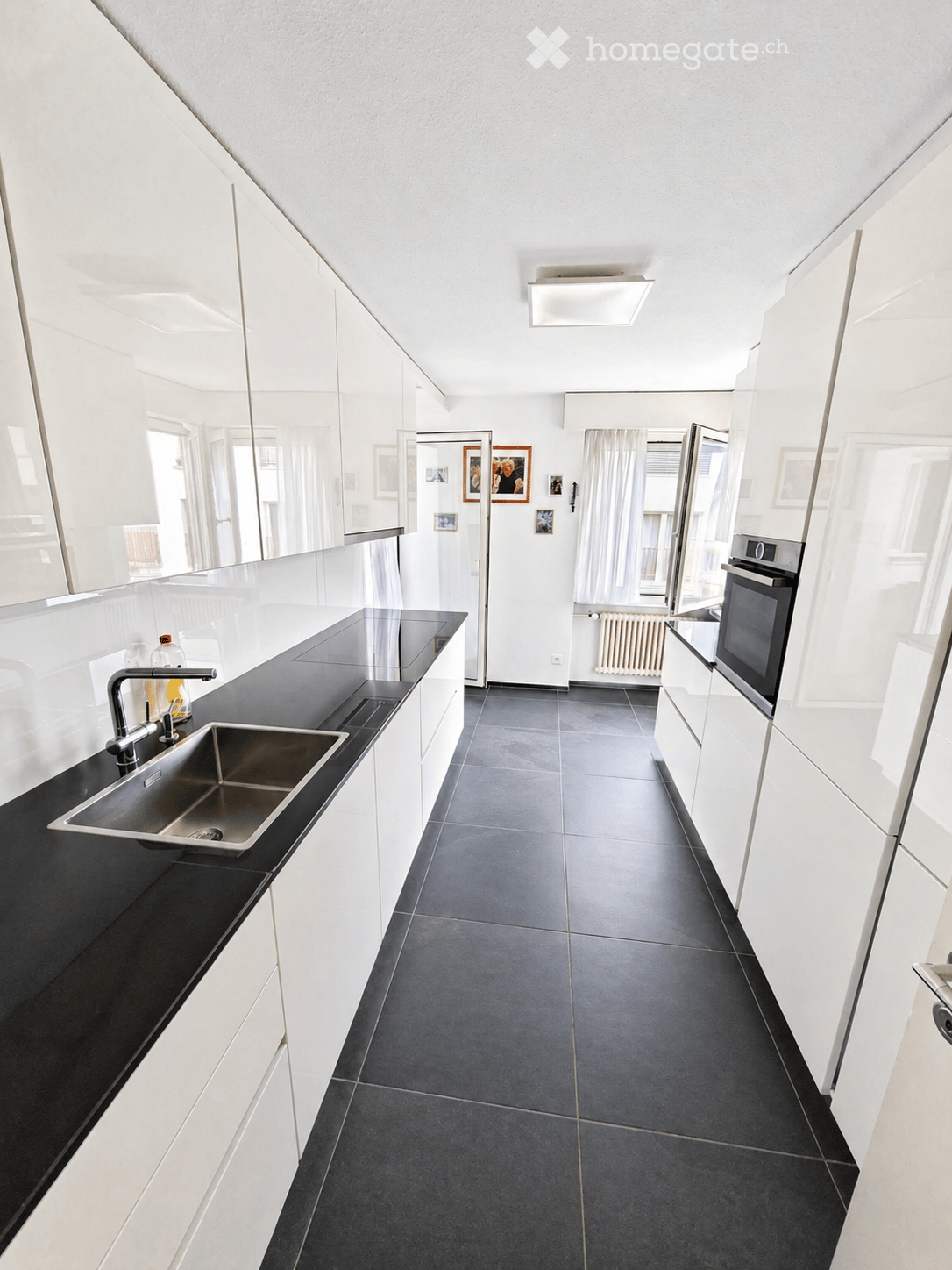 modern kitchen with white cabinets, black countertops, stainless steel sink, built-in oven, dishwasher, and a faucet