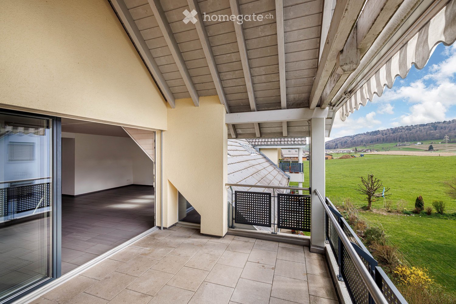 Balcony with tiled floor, glass doors, metal railings, and a view of a green field