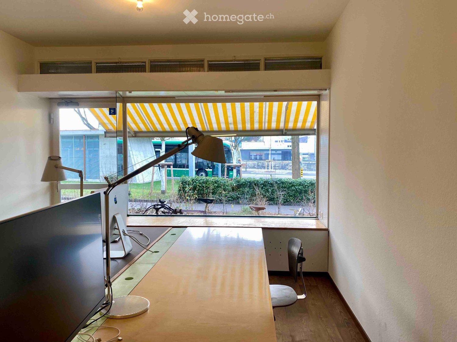 desk, chair, monitor, lamp, window with awning, bicycles outside