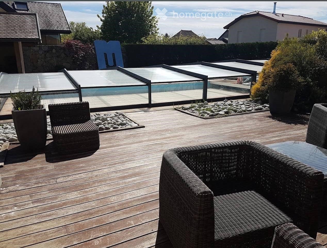 Wooden deck, wicker chairs, glass pool cover, plants, view of the sky