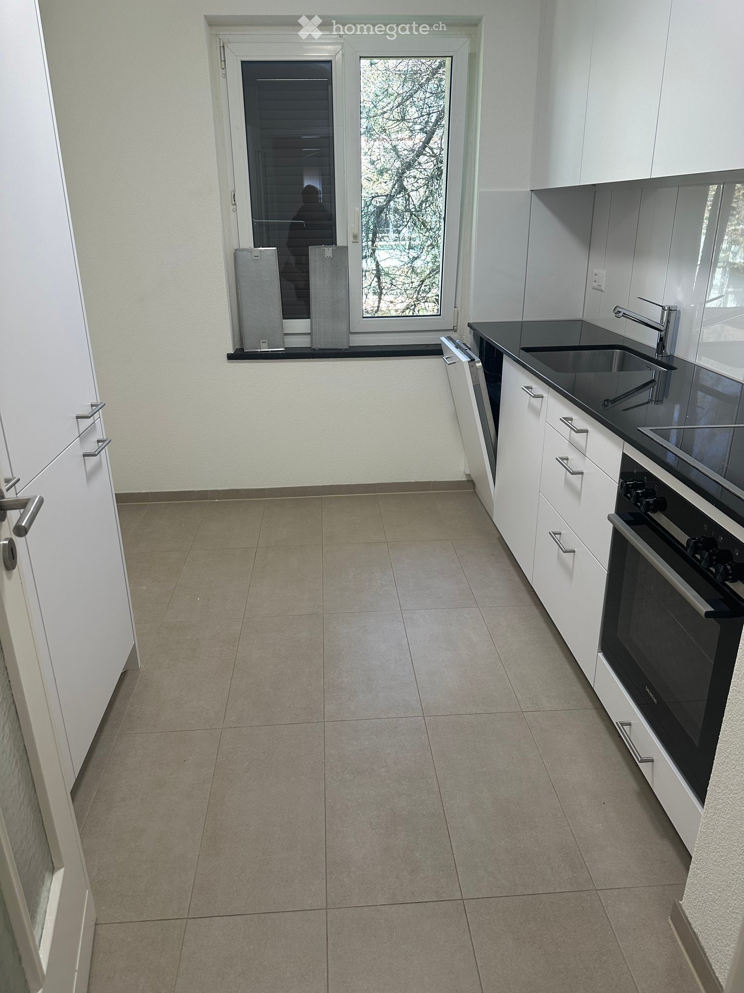 modern kitchen with white cabinets, black countertops, stainless steel sink, oven, dishwasher, and a window with blinds