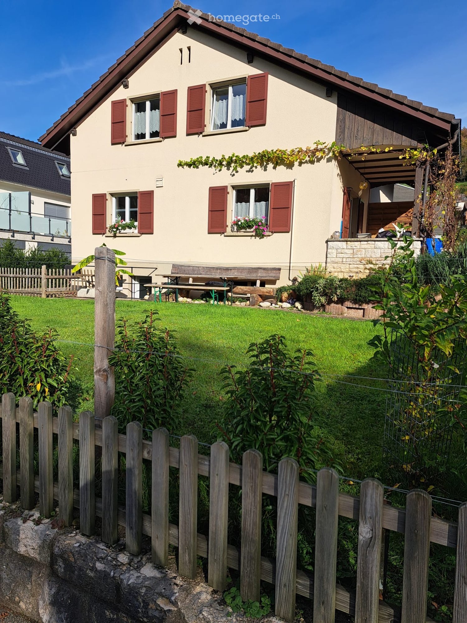 2 story house, beige exterior, red shutters, wooden bench, garden, green lawn, wooden fence