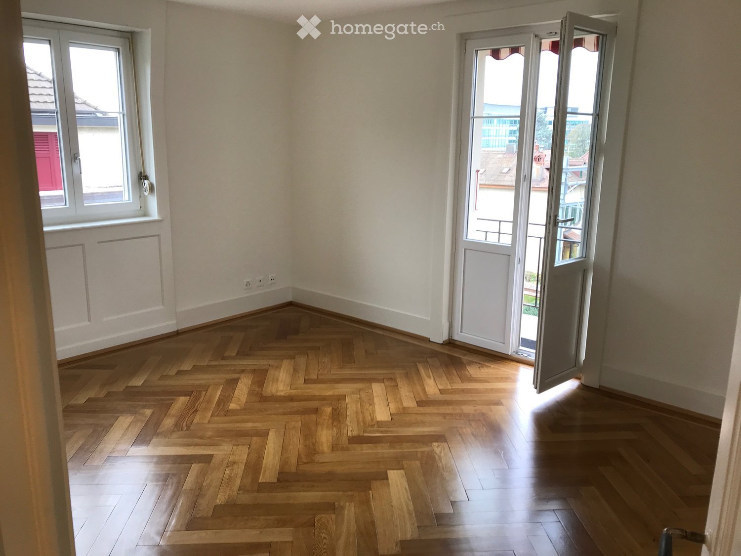 herringbone parquet flooring, white walls, glass doors leading to a balcony, two windows