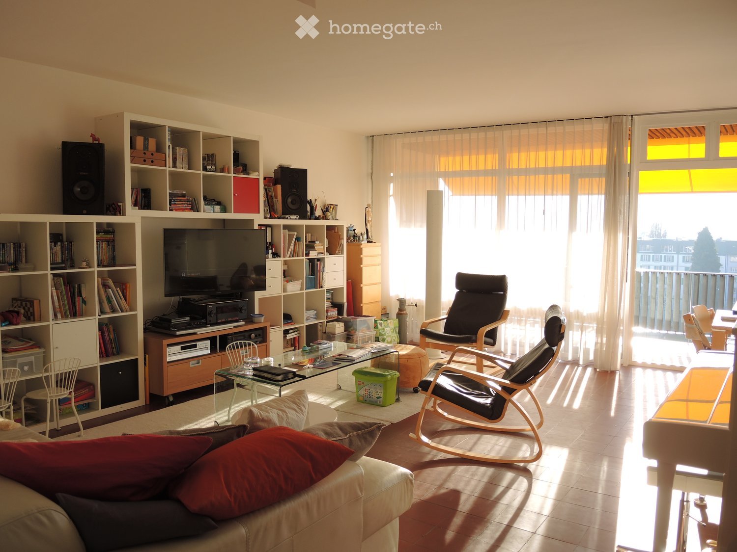 large living room, white couch, white shelves, TV, speakers, glass coffee table, wooden chairs, balcony, large windows