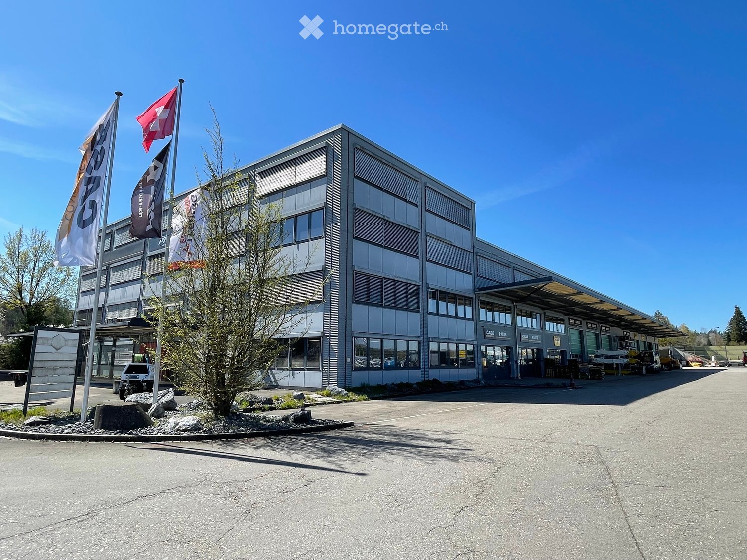 modern office building, gray exterior, multiple windows, large parking area, flags