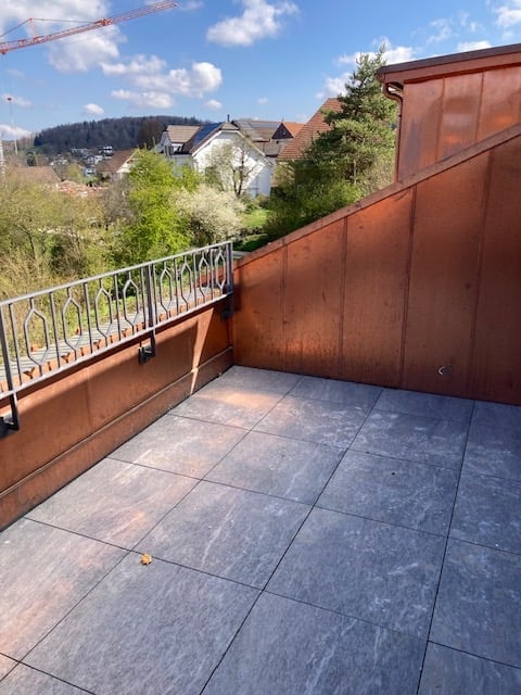 Balcony with tiled floor, metal railing, brown wall, and a view of the surroundings