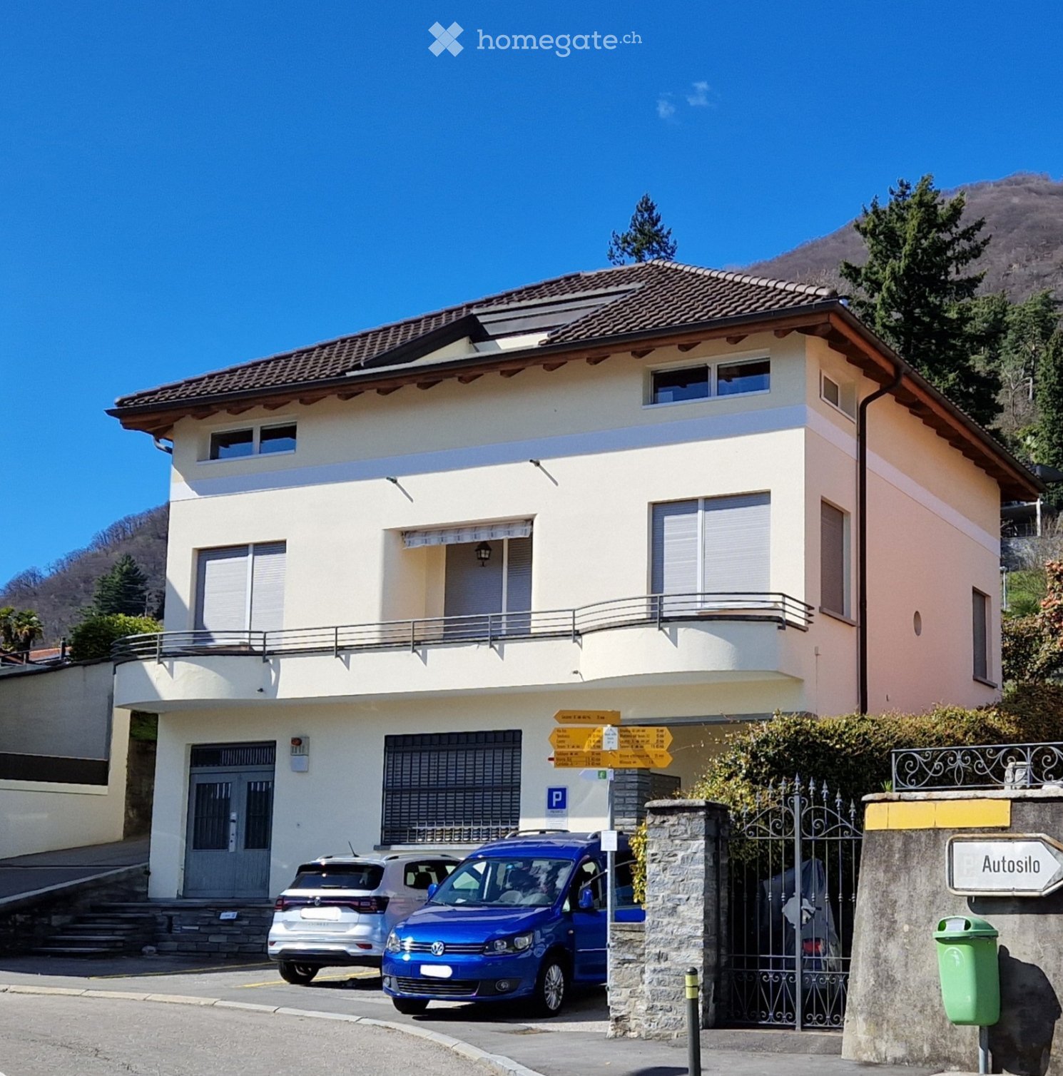 2 story house, brown roof, white walls, balcony, 2 cars parked in front