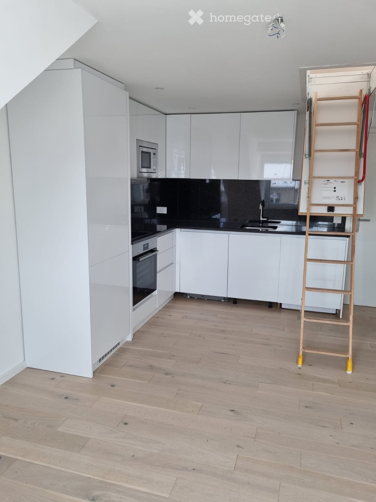 modern kitchen with white cabinets, black countertops, wooden floor, built-in microwave, oven, sink, faucet, ladder