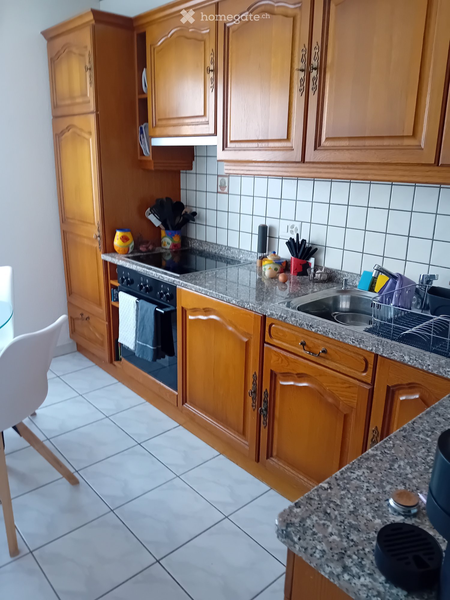 kitchen with wooden cabinets, granite countertop, electric stove, oven, sink, dish rack, white tiles, white chair