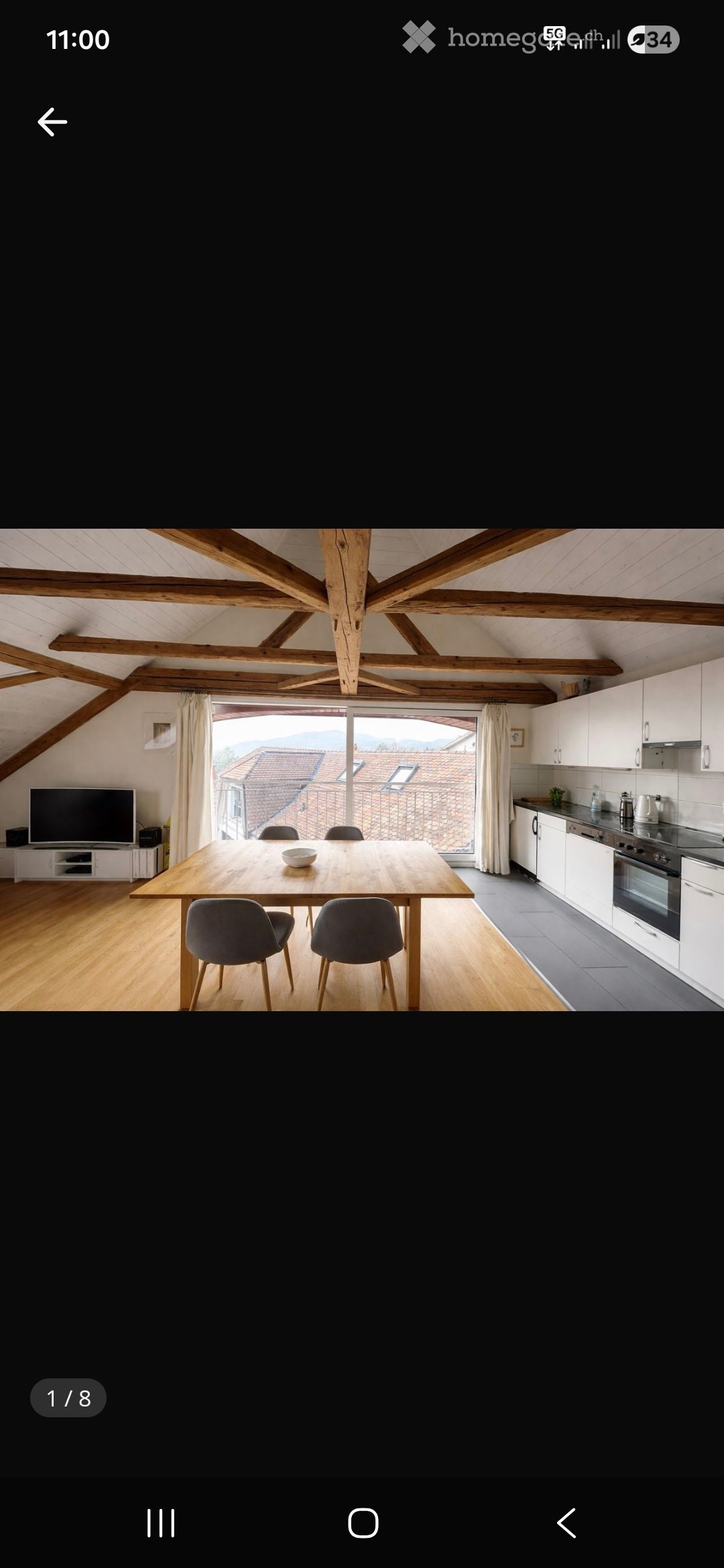 Dining area with wooden table, chairs, TV, kitchen with appliances, wooden beams