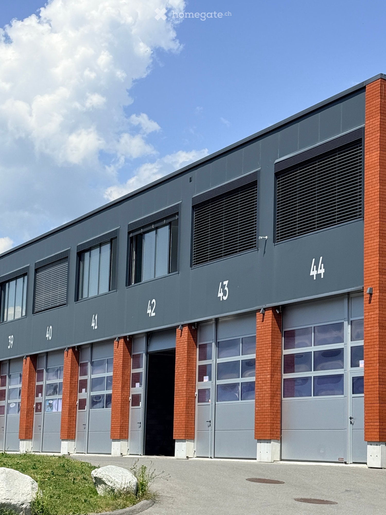 Modern industrial-style building with multiple garage doors, numbered units (39-44), and brick accents.