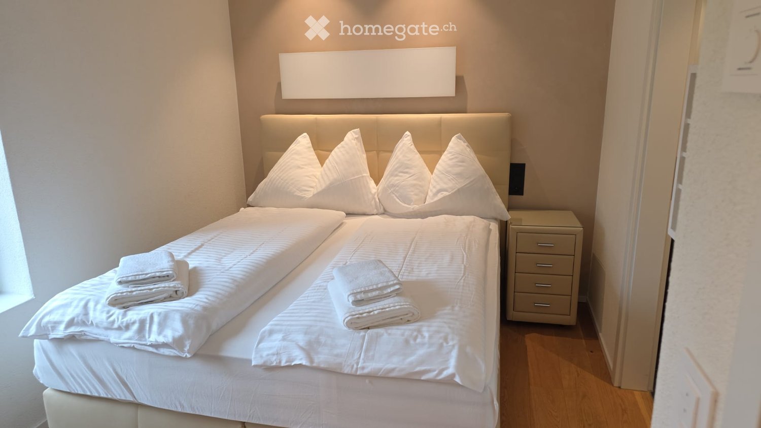 Double bed, white linens, white pillows, nightstand, wooden floor, white walls