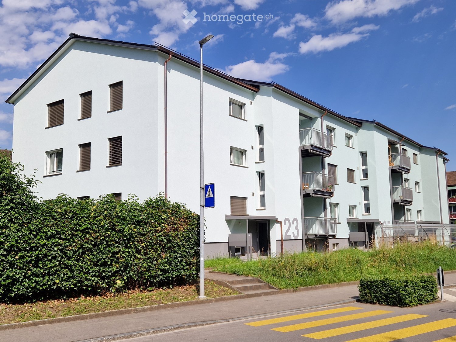 3-story apartment building, white exterior, multiple windows, balconies, street light, green bushes, grass