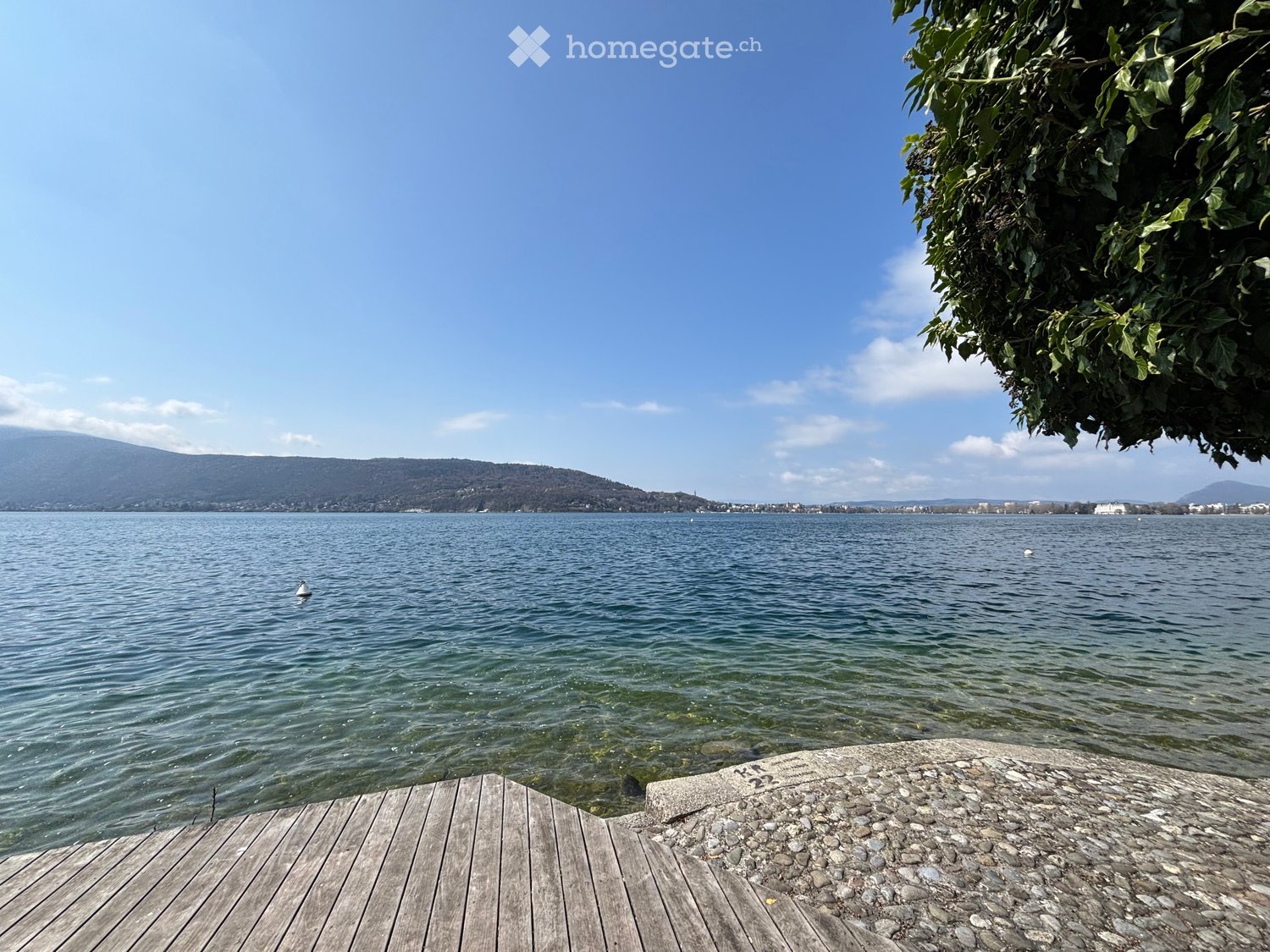 wooden deck, pebbled ground, lake, mountains, clear sky