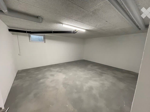 Empty room with white walls, gray floor, small window, and a ceiling light