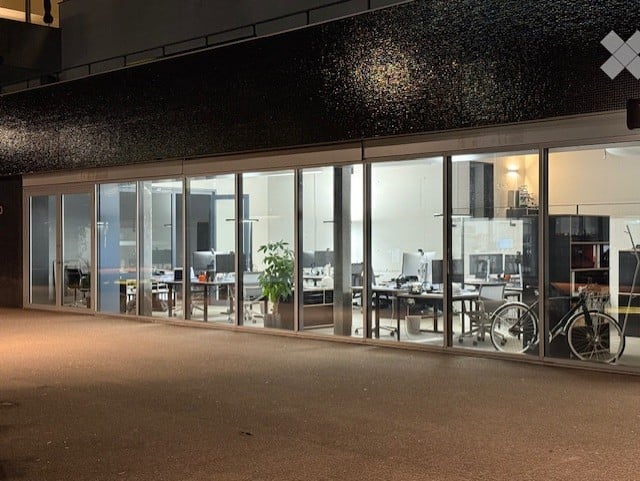modern office building with glass walls, interior with desks, chairs, and plants, bicycle parked outside