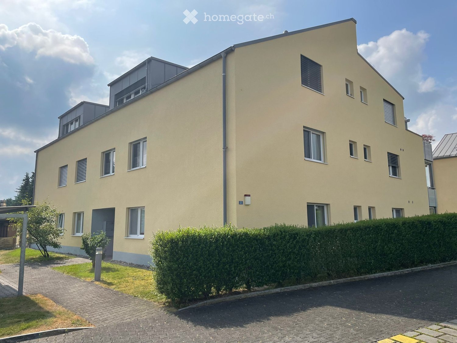 3 story building, yellow exterior, multiple windows, brick walkway, hedges, small garden