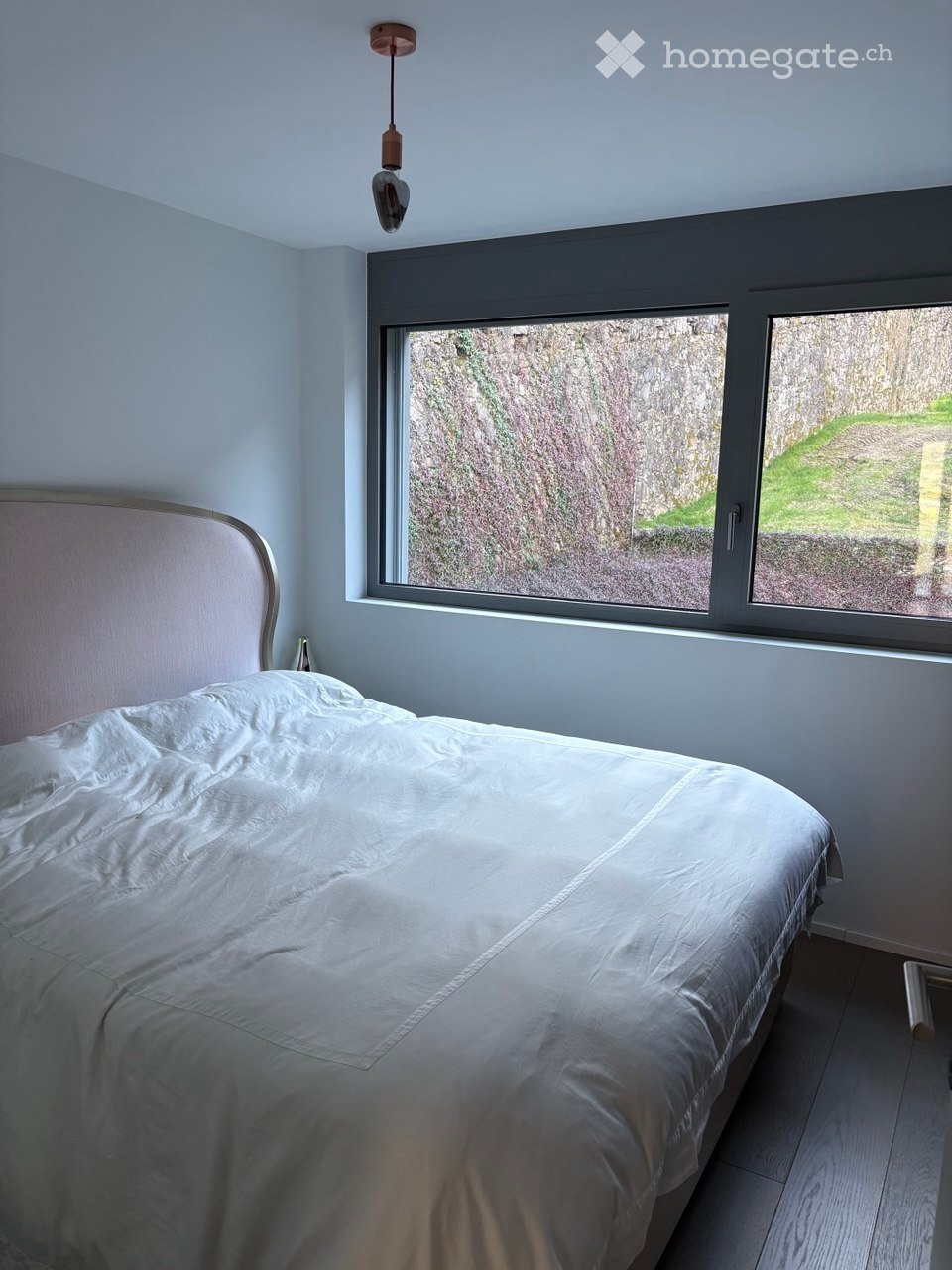 Bedroom with a bed, white bedding, large window, view of greenery outside