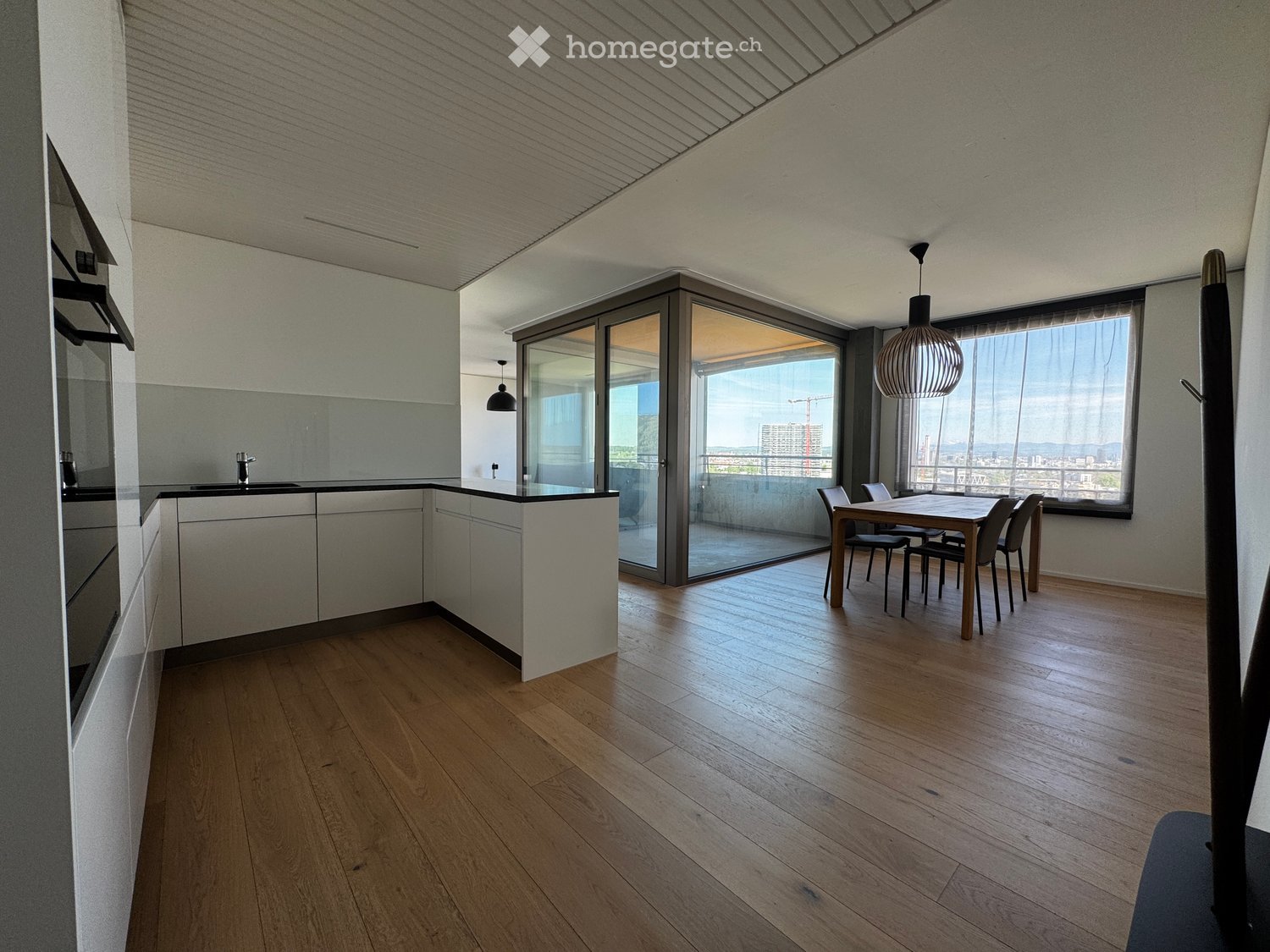 Modern kitchen with wooden floor, white cabinets, and a dining area with a table and chairs.