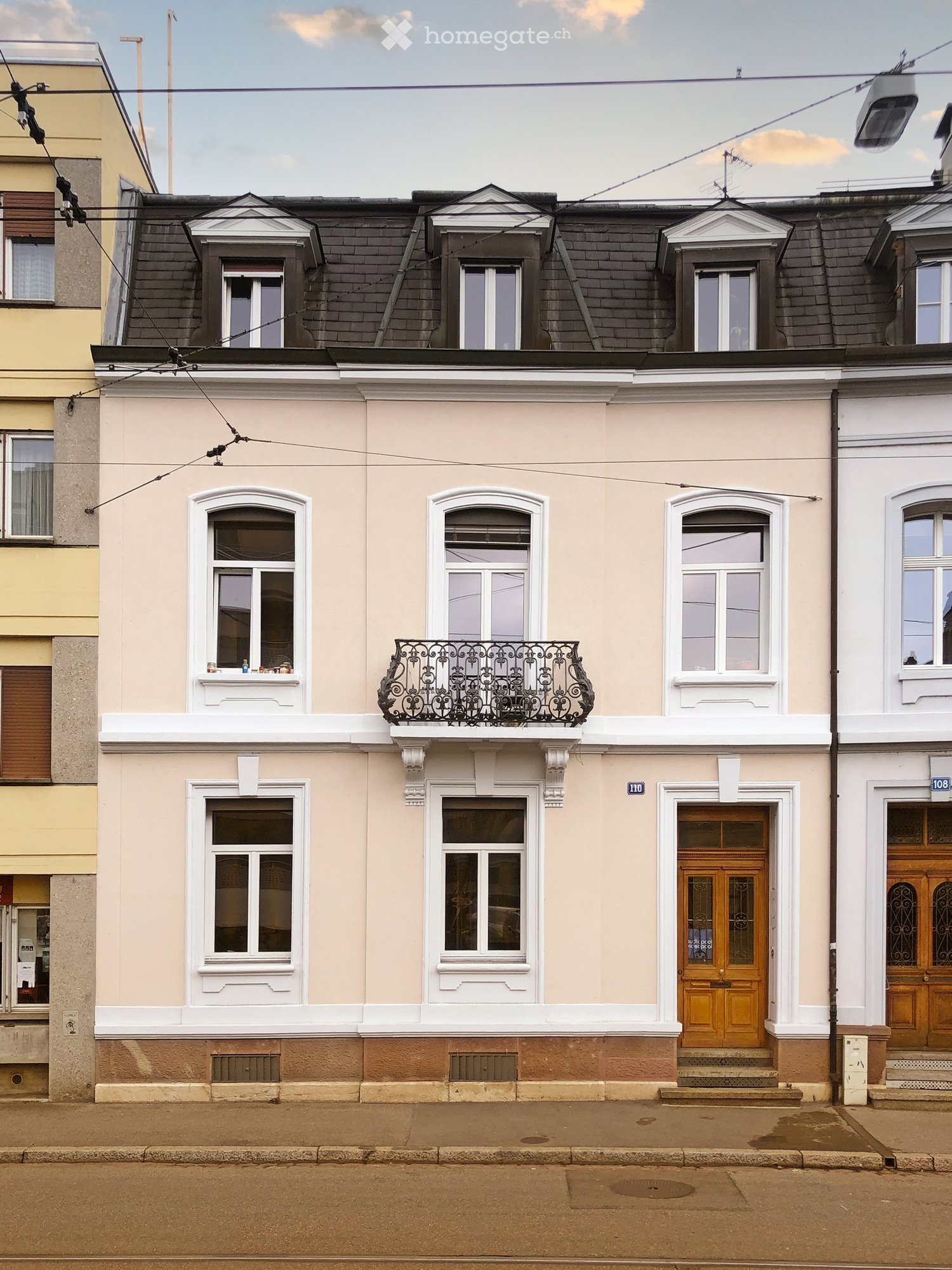 3 story house, beige and white facade, black roof, wooden doors, balcony, windows