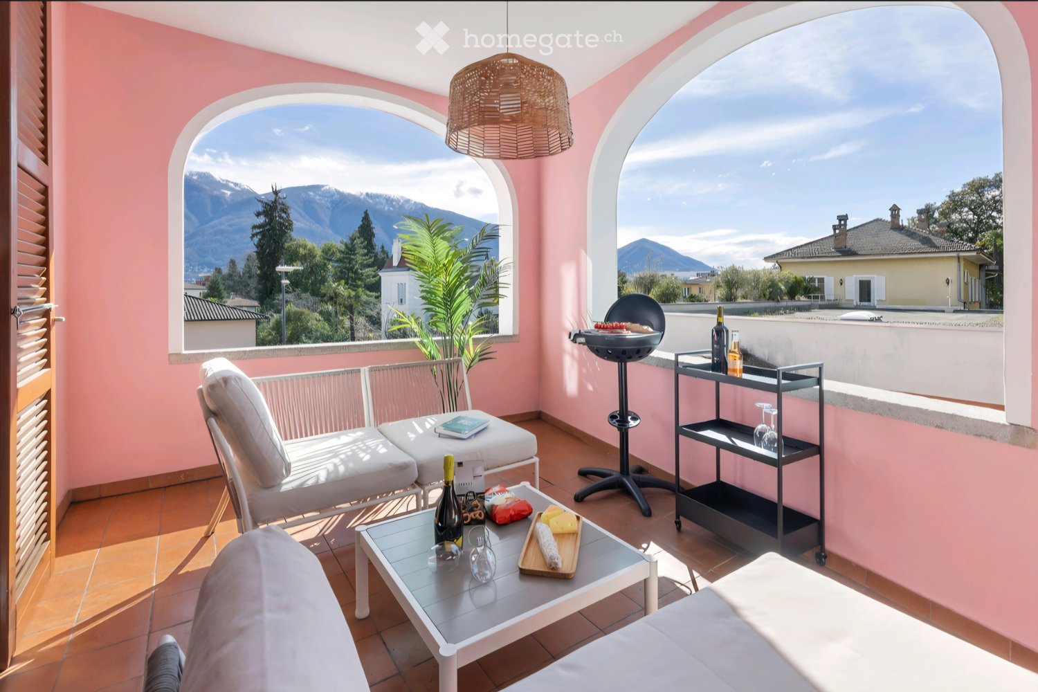 balcony, pink walls, white furniture, table with wine and cheese, outdoor grill, mountain view