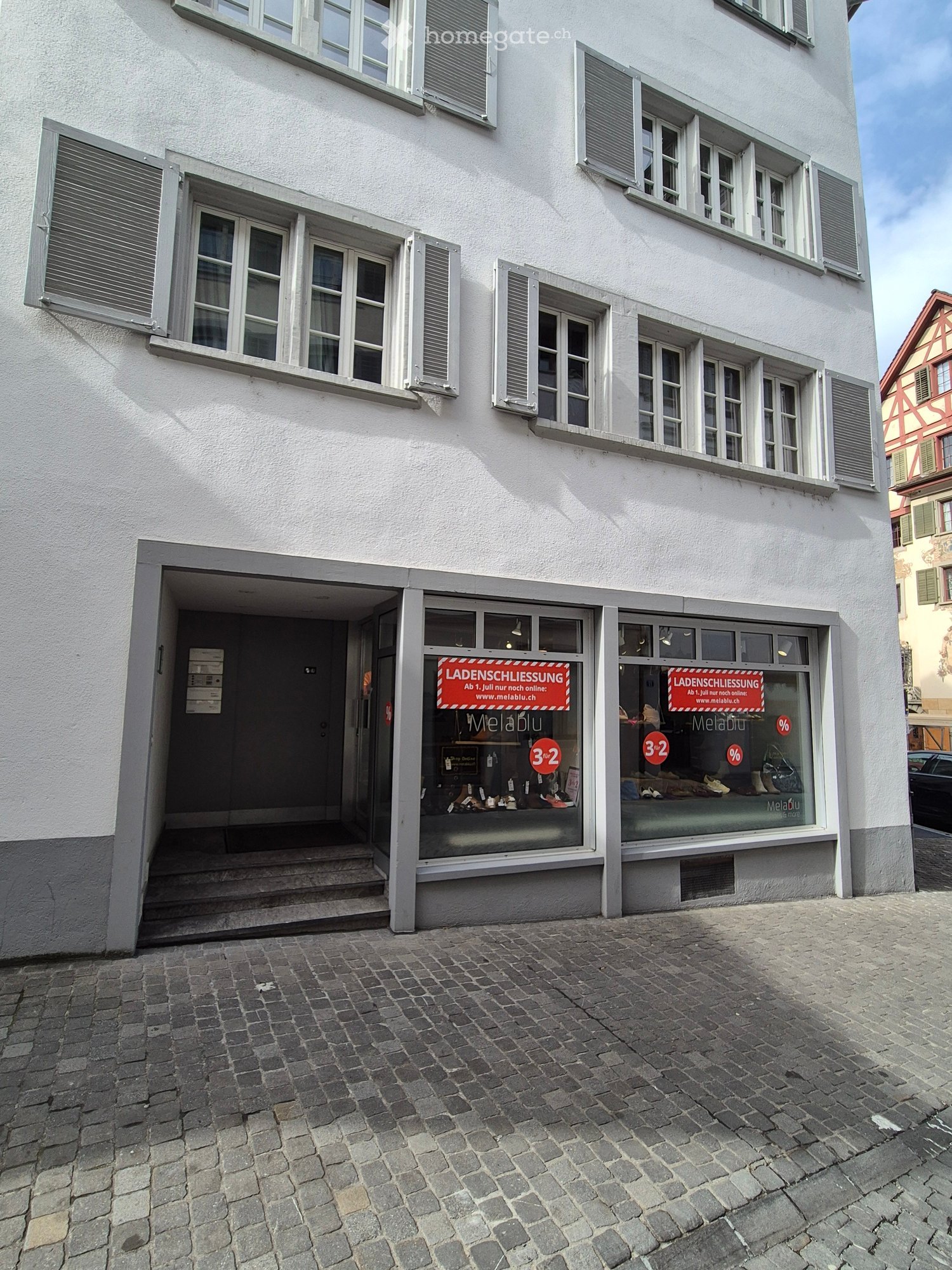 White building with multiple windows, entrance with steps, sign indicating store closure