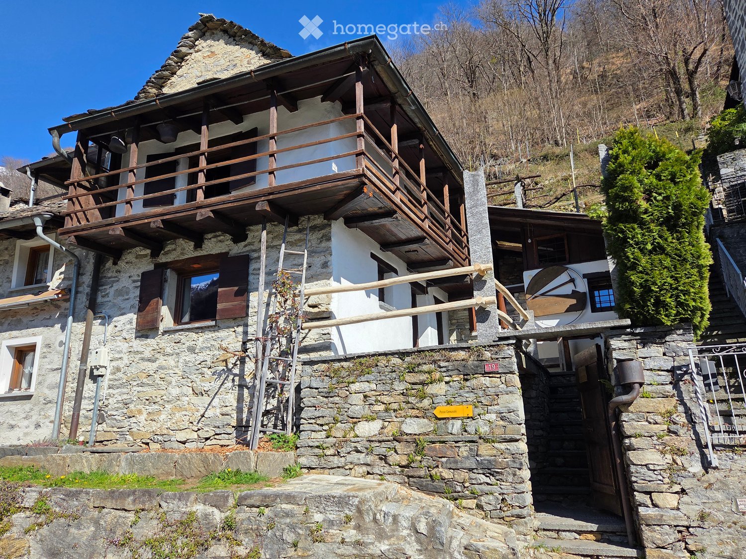 Stone house, wooden balcony, multiple windows, wooden ladder, stone wall, entrance door