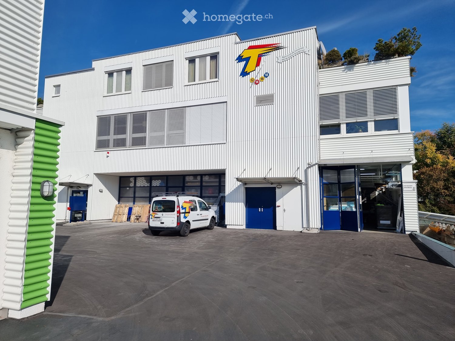 white building, blue doors, white van parked in front, logo on the wall
