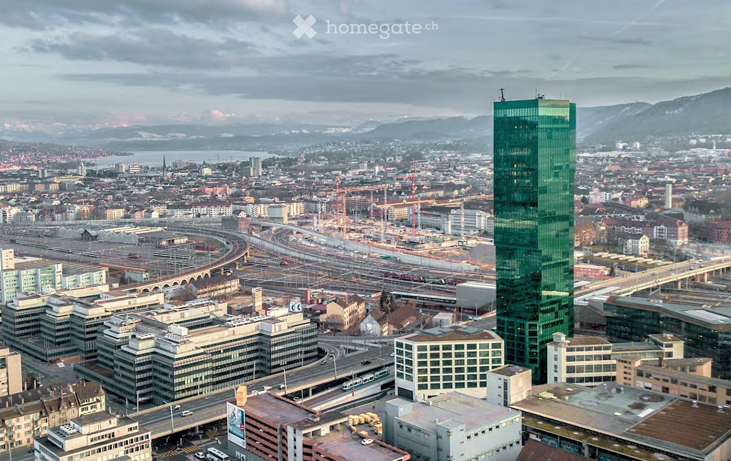 Aerial view of a city with many buildings, a prominent green skyscraper, and a highway with multiple lanes.