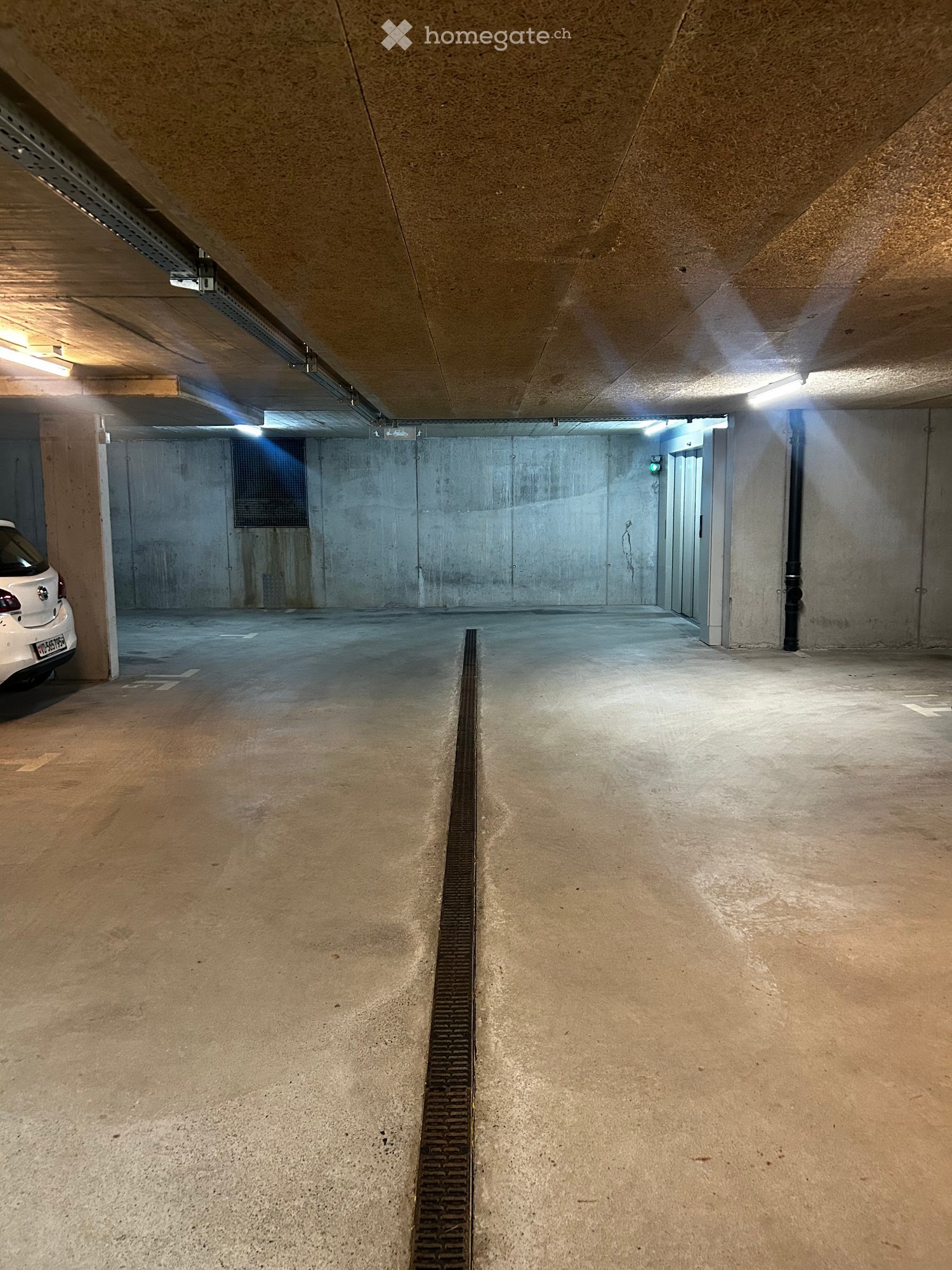 Empty parking lot with concrete floor, metal grates, and ceiling lights