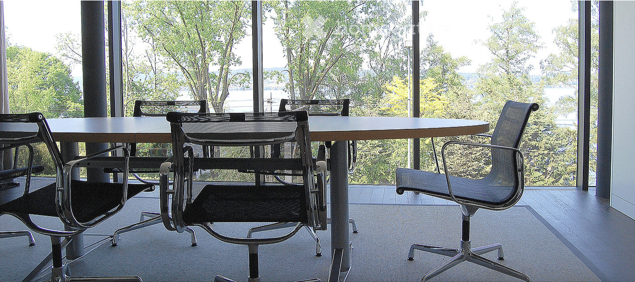 modern office room, large windows, round table, black chairs, view of trees and water