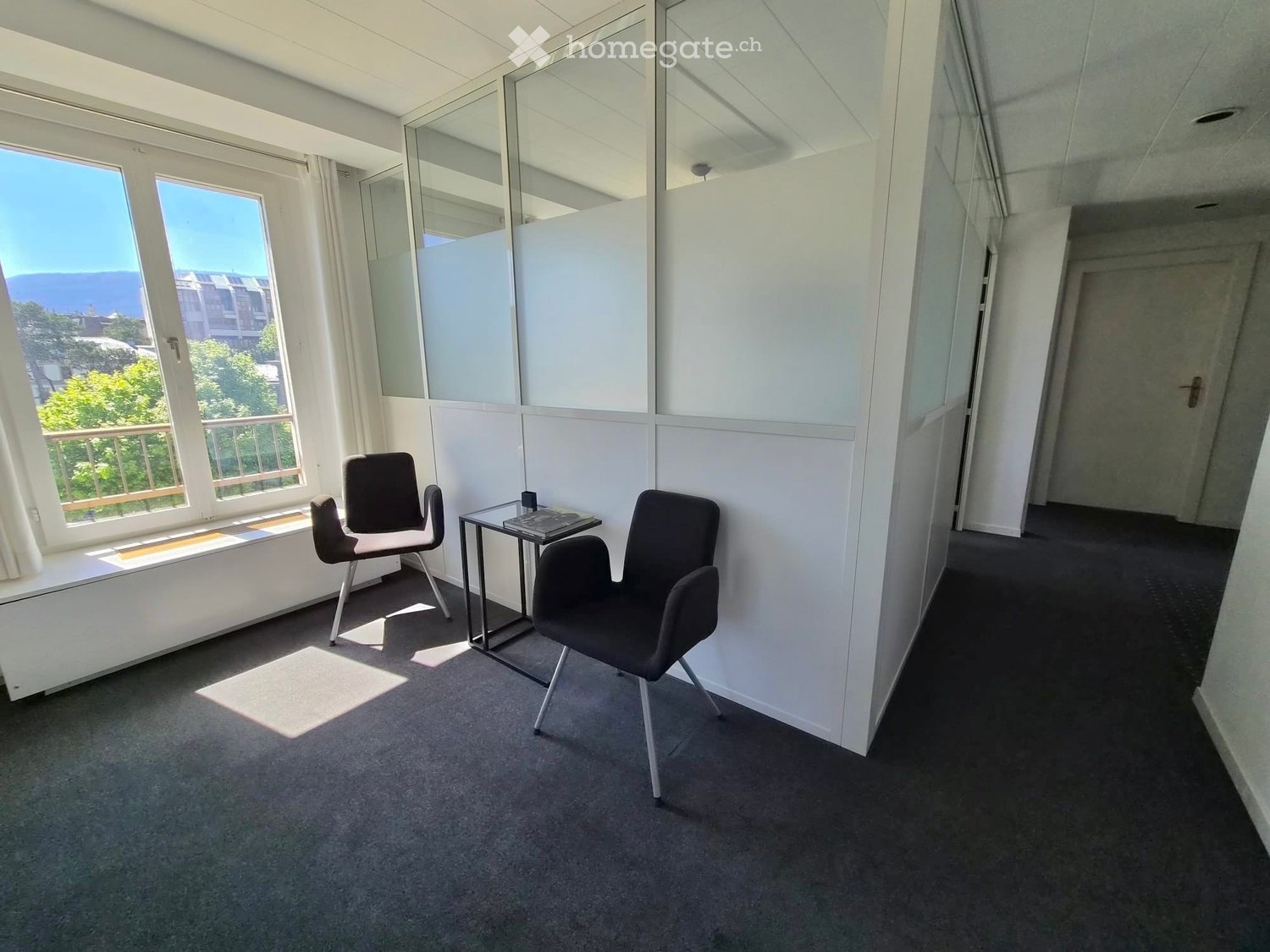 A small, modern room with two black chairs and a small glass table near a large window offering a scenic view.
