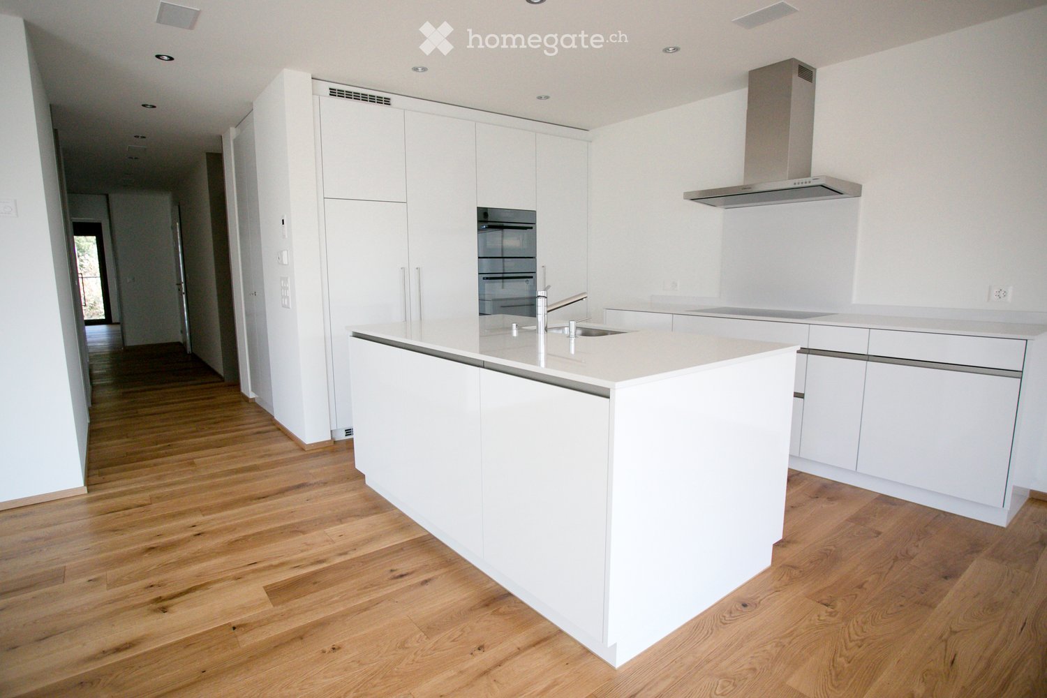 modern kitchen with white cabinets, wooden floor, central island with sink, oven, and extractor hood
