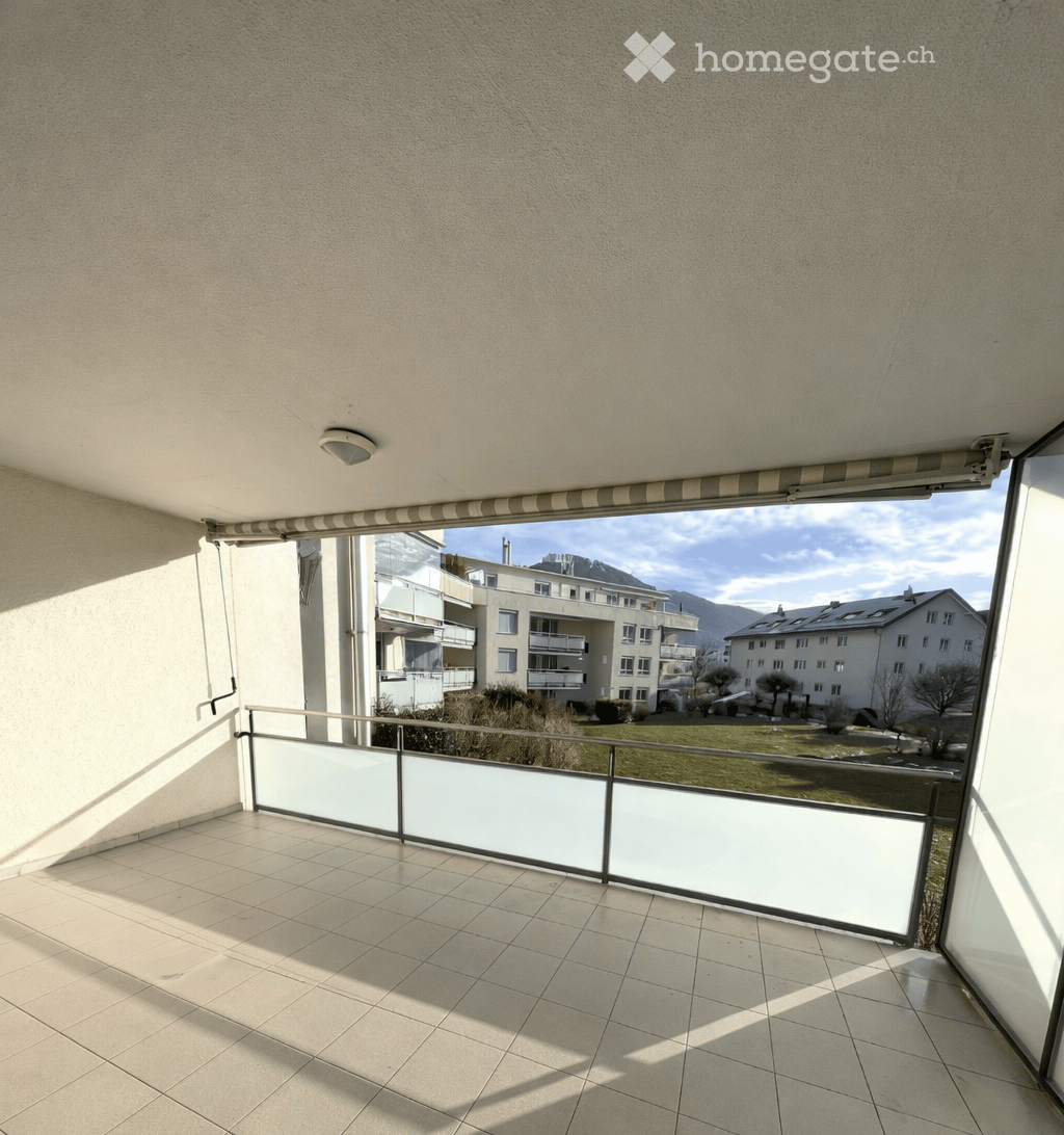 empty balcony with tiled floor, glass railing, openable glass door, view of a grassy area and buildings