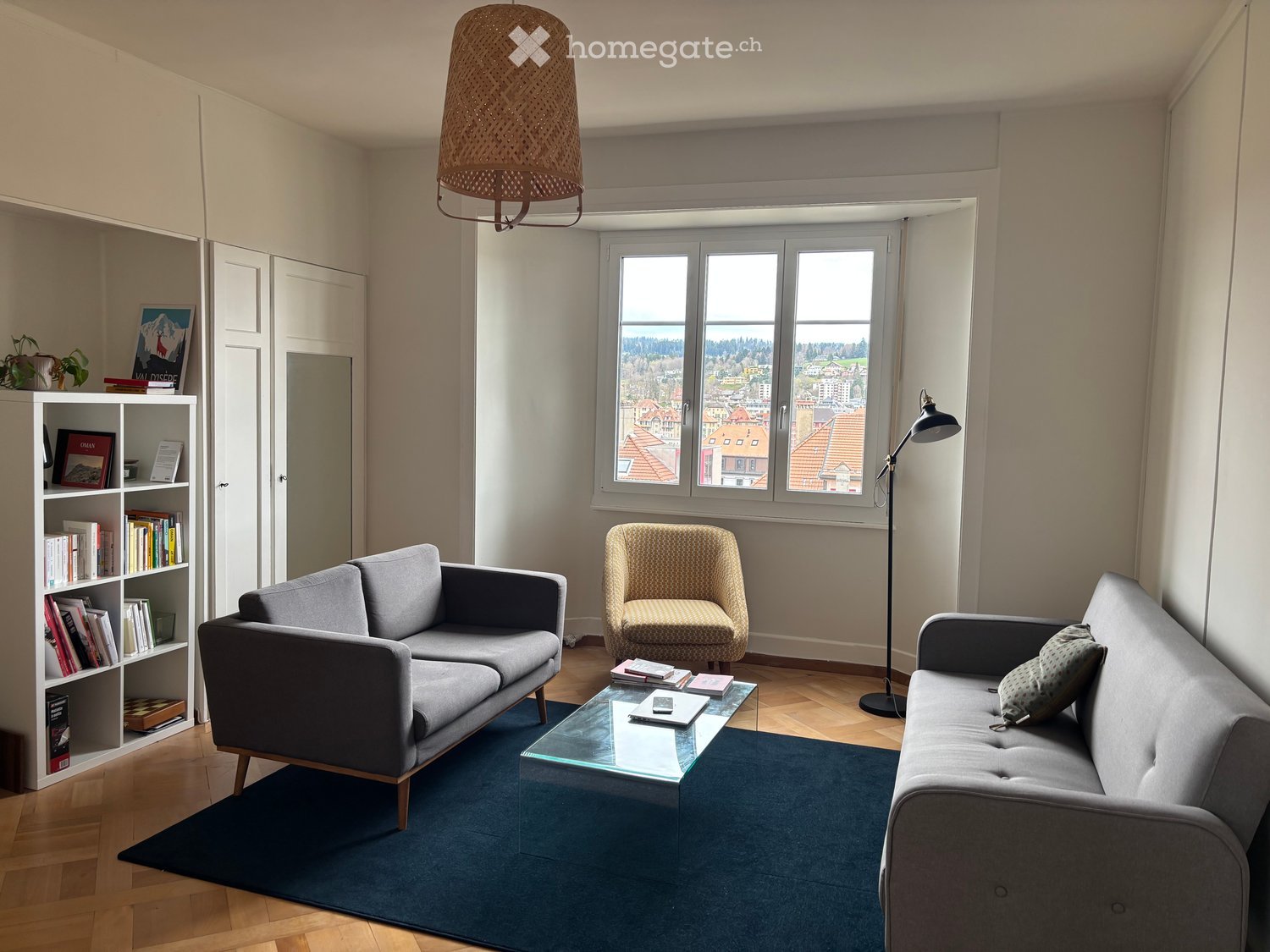 living room with two sofas, glass coffee table, armchair, floor lamp, bookshelf, rug, wooden floor, large window
