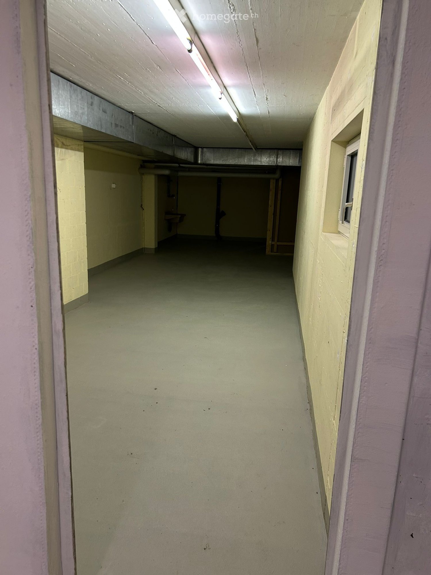 Empty basement room with concrete floor, yellow walls, a window, and a sink.
