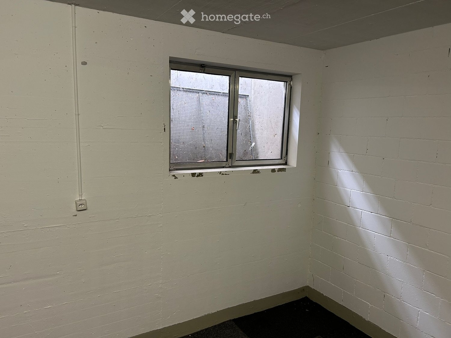 Empty room with white walls, a single window, and a dark floor. No furniture or equipment present.